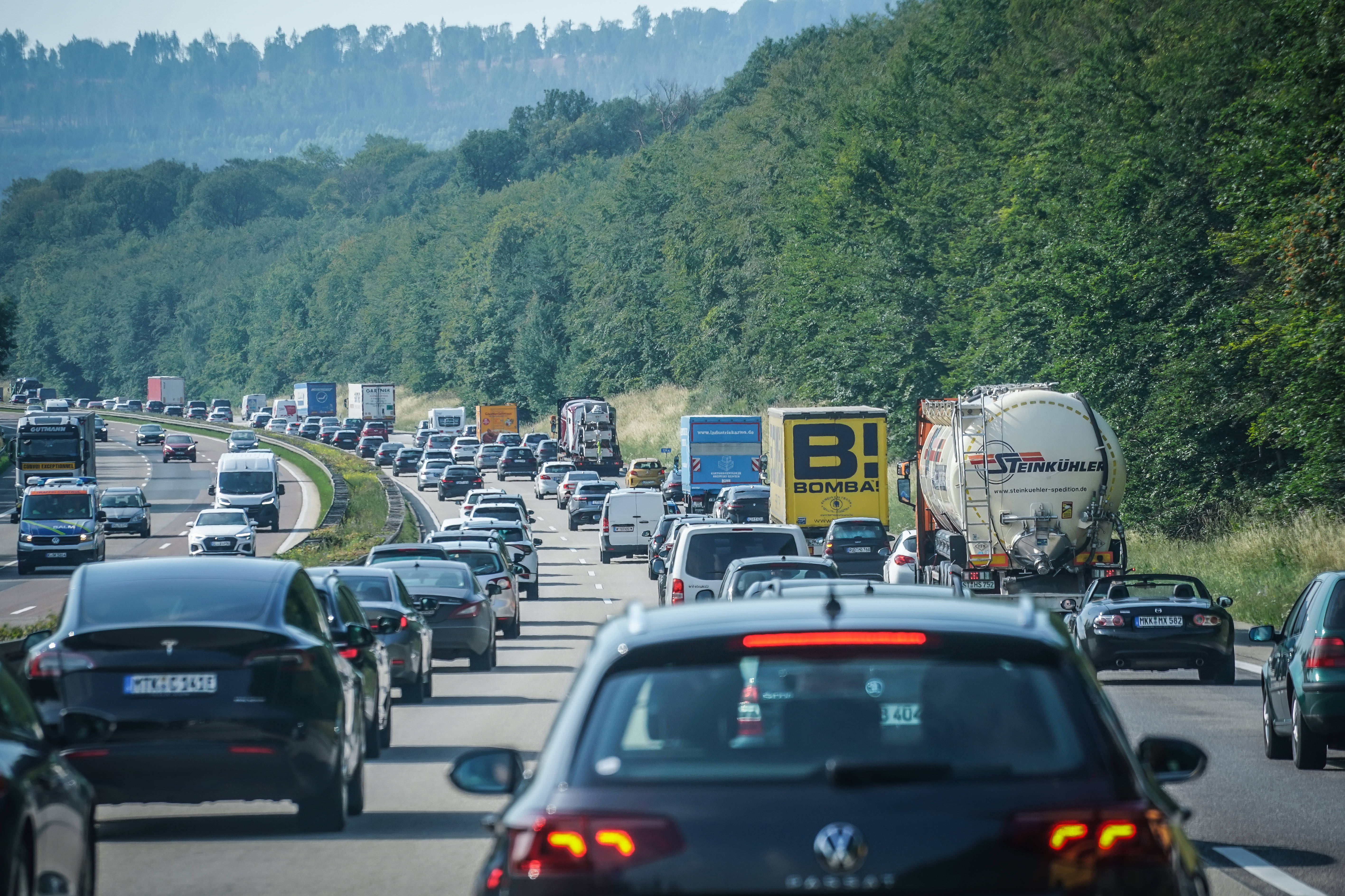 Autos stehen oder fahren auf einer Autobahn vor grün bewaldeten Hängen