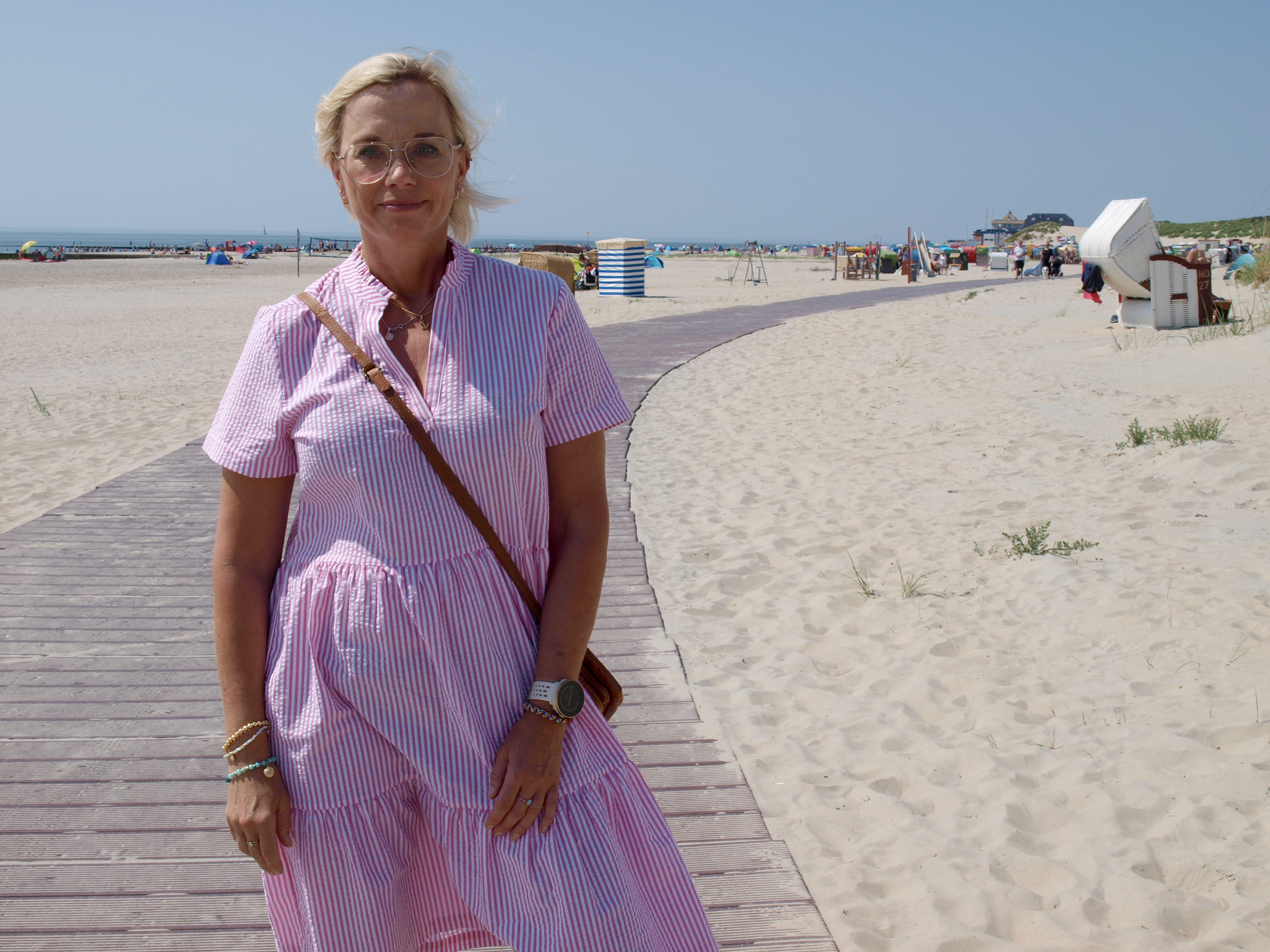 Frau mit rot-weißem Kleid steht am Strand