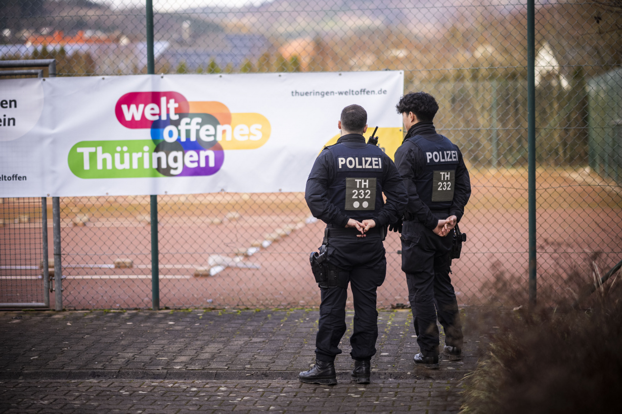 Polizisten bewachen ein Betriebsgelände vor einem Werbetransparent des Landes Thüringen, das für ein weltoffenes Land wirbt.